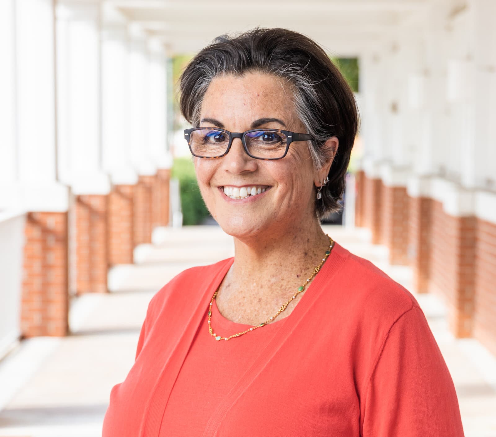 Leigh Ann Kingsbury, smiling, standing in a sunlit brick colonnade